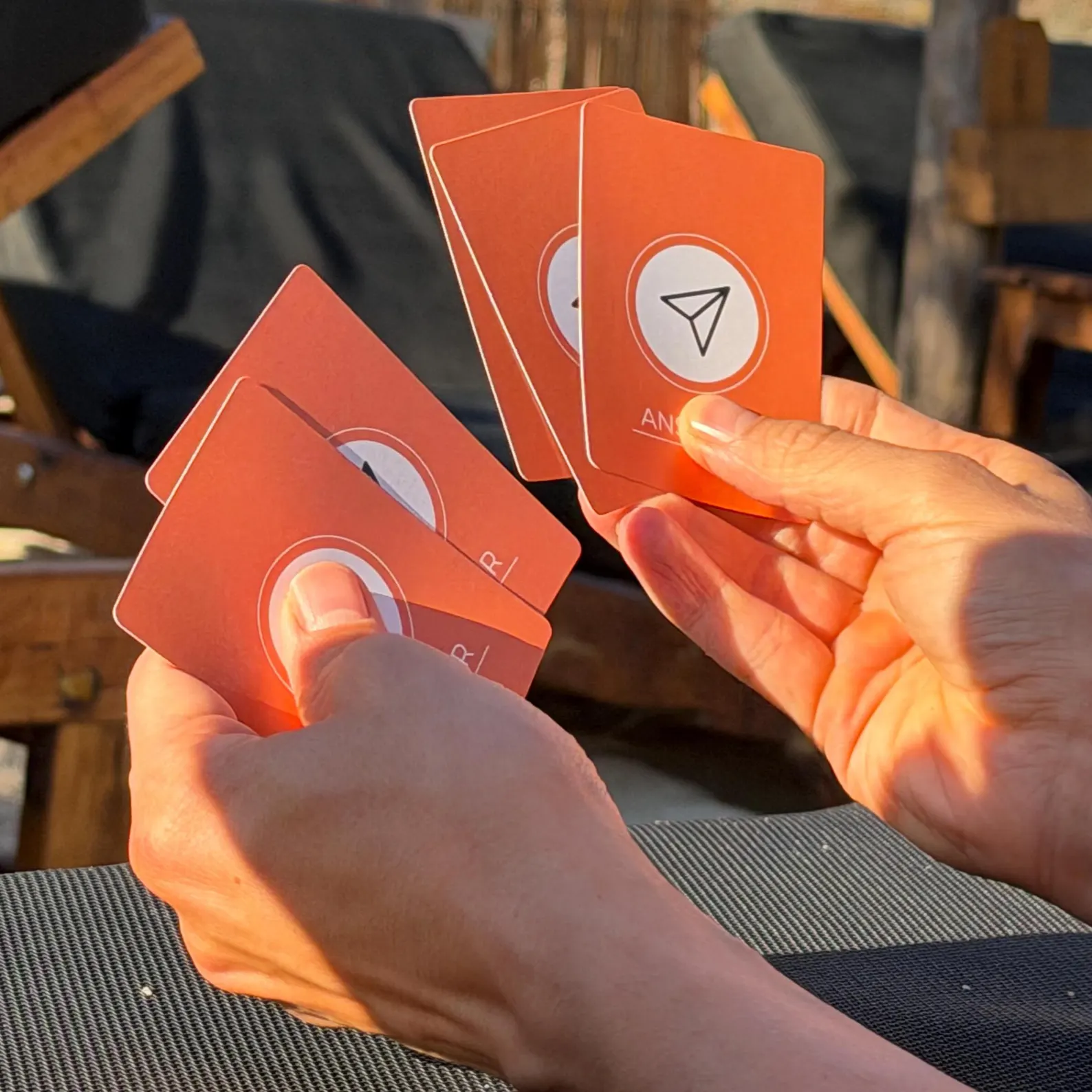 Two hands holding orange Headless Torsos ANSWER cards in golden evening light